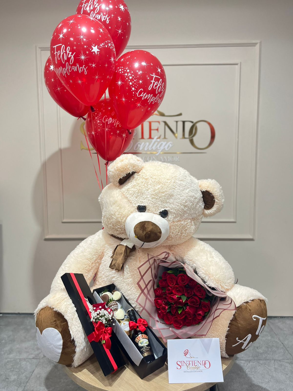 Oso de peluche gigante, con bouquet de rosas, caja de fresas con chocolate, botella de Bailey's y globos con helio