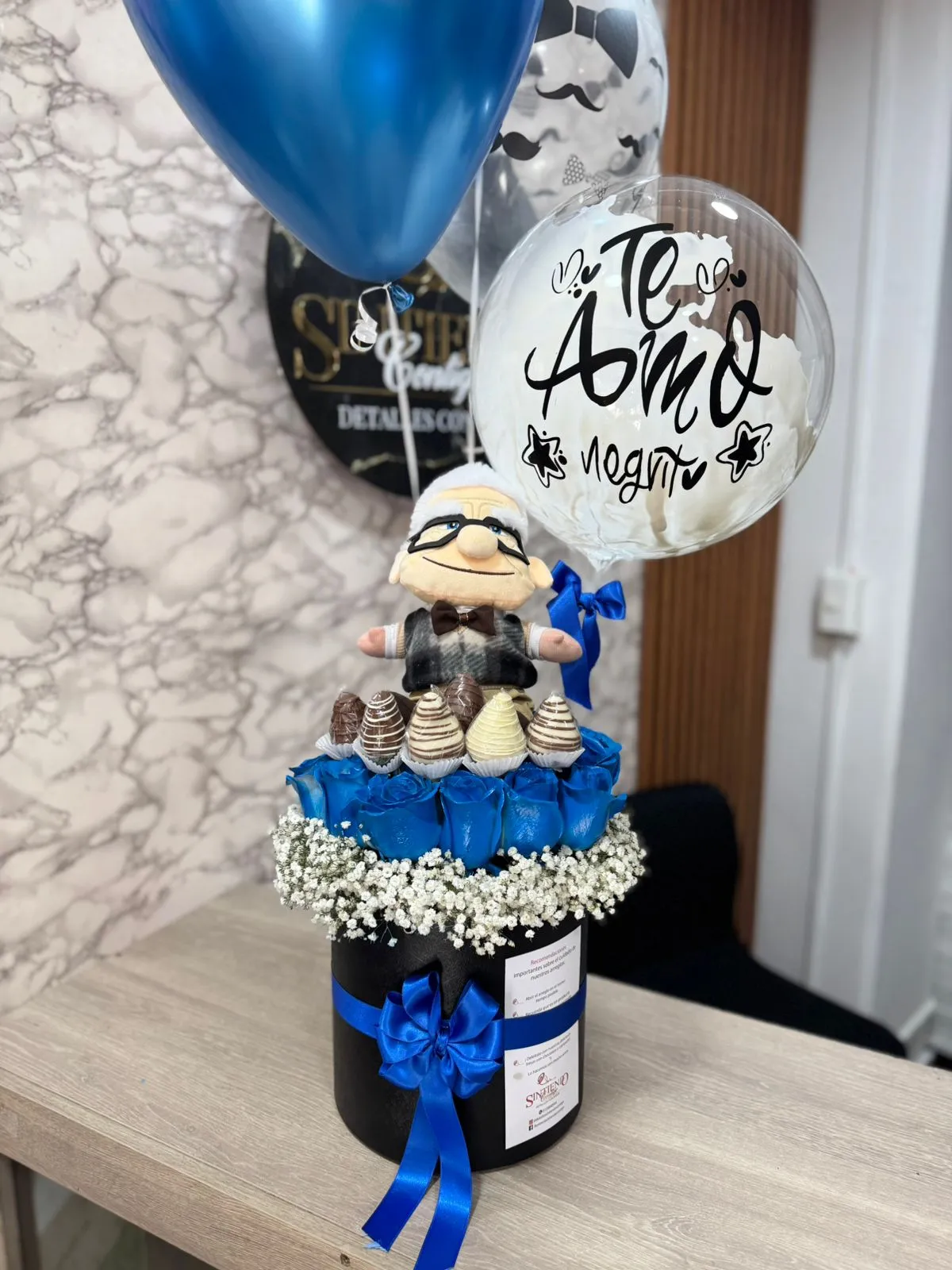 Cilindro con rosas azules, fresas con chocolate, peluche y globos con helio